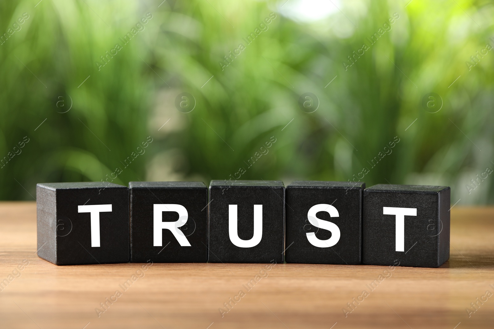 Photo of Word Trust made of black cubes on wooden table against blurred background