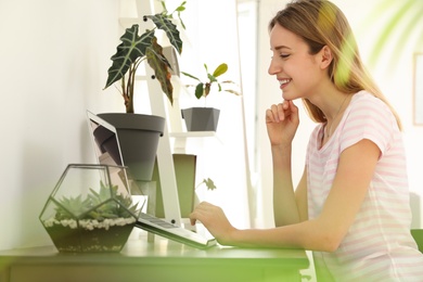 Photo of Young woman using laptop at home, space for text. Trendy room interior with plants