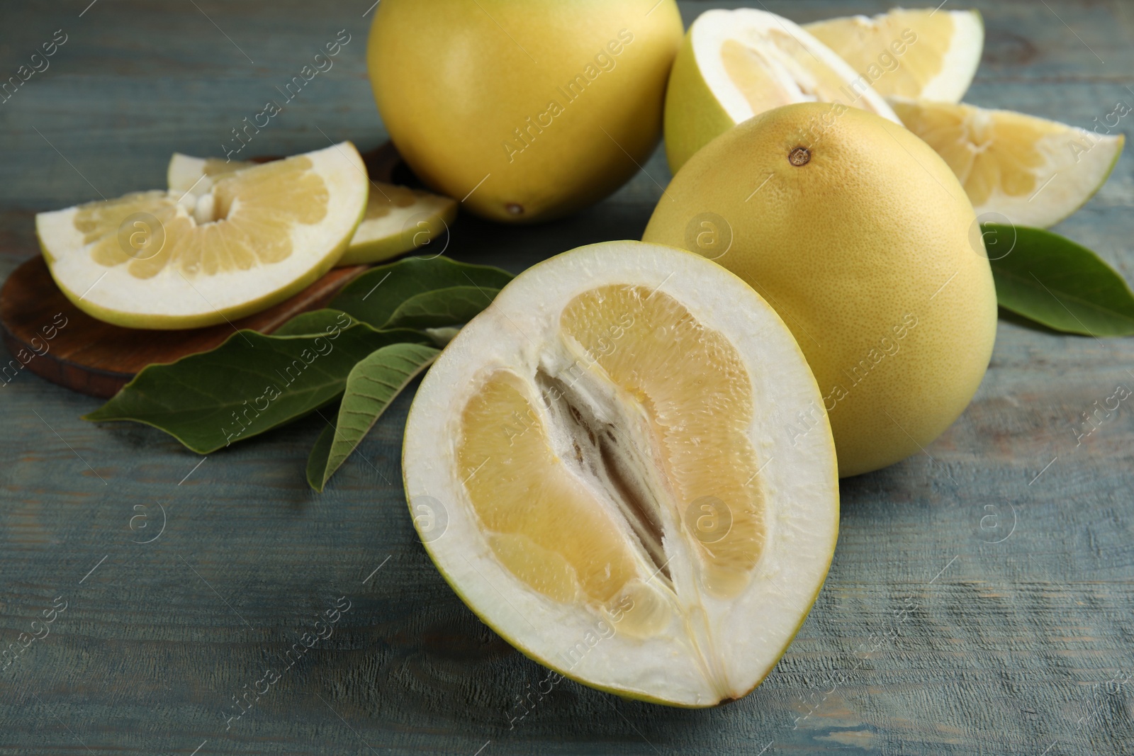 Photo of Fresh cut and whole pomelo fruits with leaves on blue wooden table