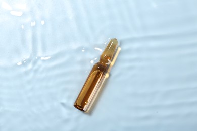 Skincare ampoule in water on light blue background, top view