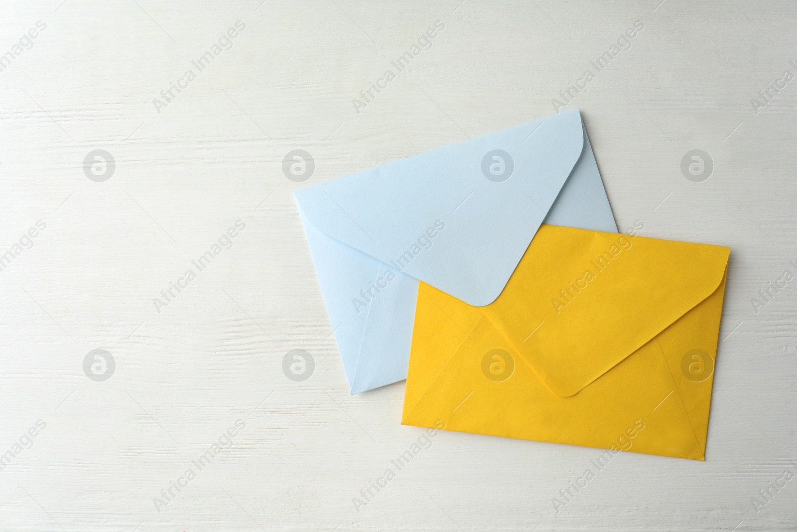 Photo of Colorful paper envelopes on white wooden table, top view. Space for text