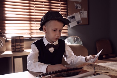 Cute little detective with fingerprints card at table in office