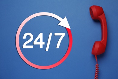 Image of 24/7 hotline service. Red handset on blue background, top view