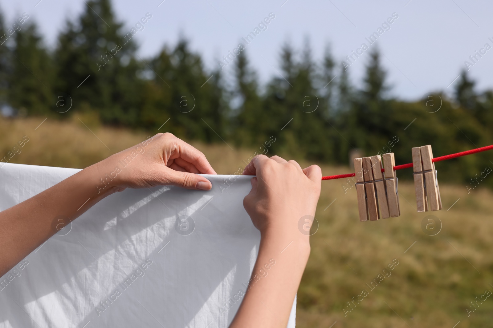 Photo of Woman hanging clean laundry with clothespins on washing line outdoors, closeup