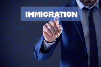 Image of Businessman touching icon with word IMMIGRATION on virtual screen against color background, closeup