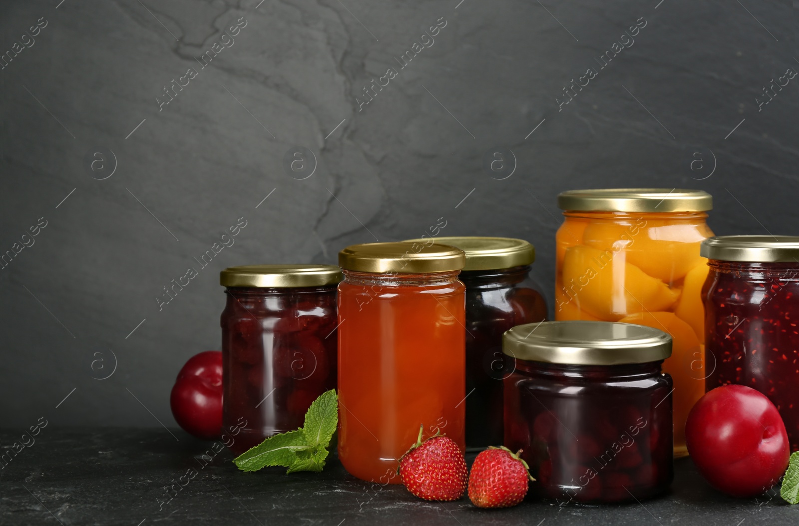 Photo of Jars of pickled fruits and jams on grey table