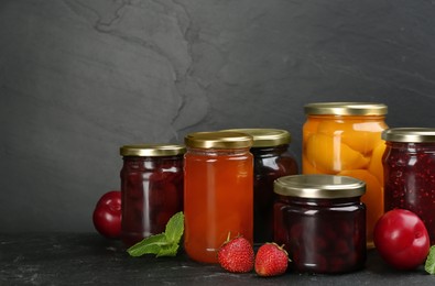 Jars of pickled fruits and jams on grey table