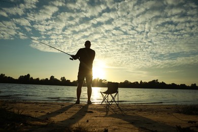 Photo of Fisherman with rod fishing at riverside at sunset, back view. Space for text