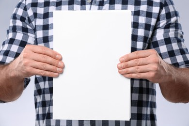 Photo of Man holding sheet of paper on light grey background, closeup. Mockup for design