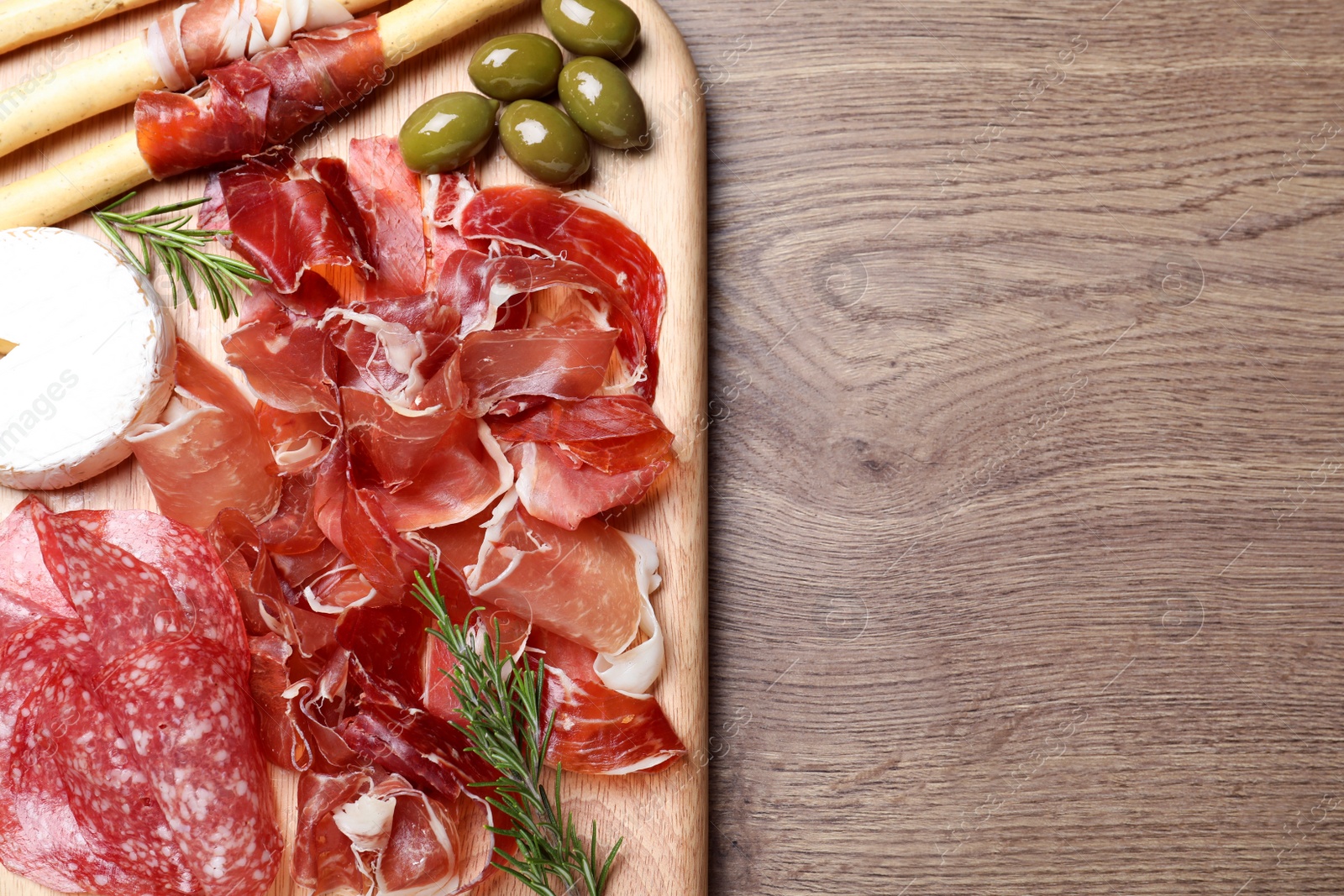 Photo of Tasty prosciutto served on wooden table, top view. Space for text