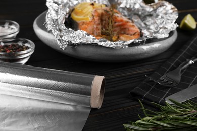 Photo of Aluminum foil and dish on black wooden table, selective focus