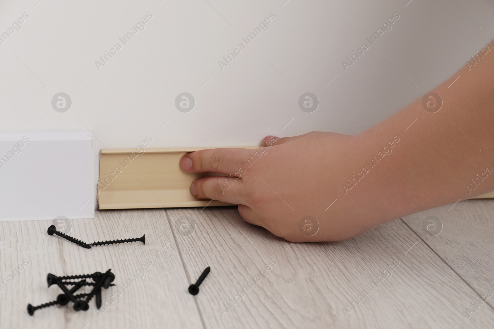 Photo of Man installing plinth on laminated floor in room, closeup