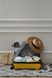 Photo of Open suitcase with summer clothes, accessories and shoes near white wall indoors, space for text