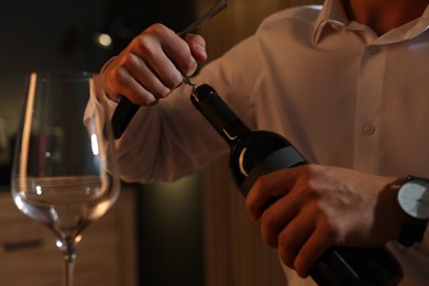 Photo of Romantic dinner. Man opening wine bottle with corkscrew indoors, closeup