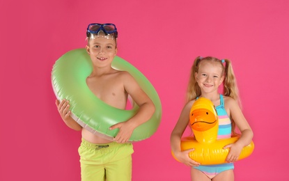 Photo of Cute little children in beachwear with bright inflatable rings on pink background