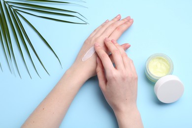 Woman applying hand cream on light blue background, top view