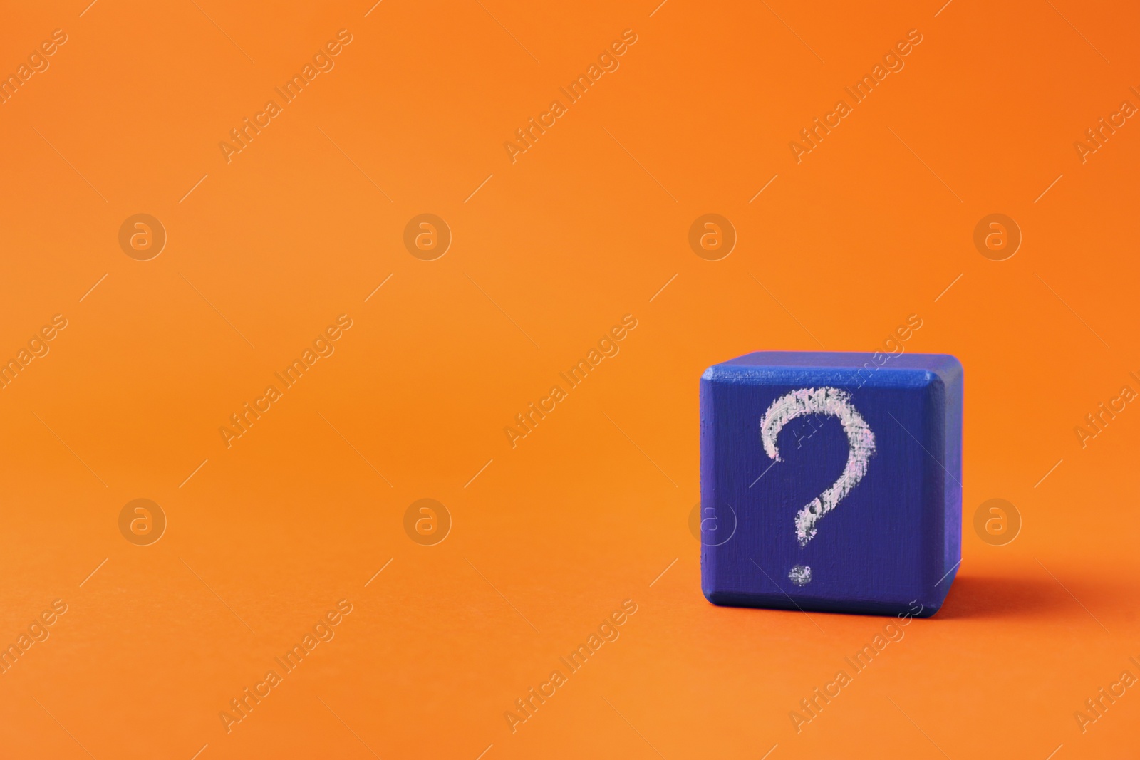 Photo of Blue wooden cube with question mark on orange background. Space for text