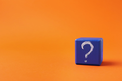 Blue wooden cube with question mark on orange background. Space for text