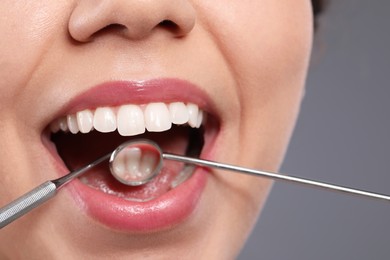 Examining woman's teeth with dentist's mirror on grey background, closeup