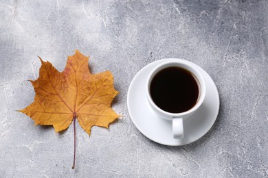 Photo of Cup of hot drink and autumn leaf on light grey textured table, above view