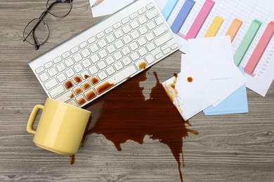 Cup of coffee spilled over computer keyboard on wooden office desk, flat lay