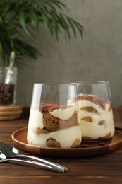 Delicious tiramisu in glasses and spoons on wooden table, closeup