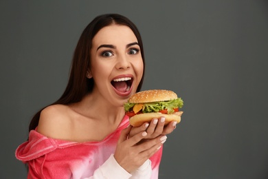 Photo of Young woman eating tasty burger on grey background. Space for text