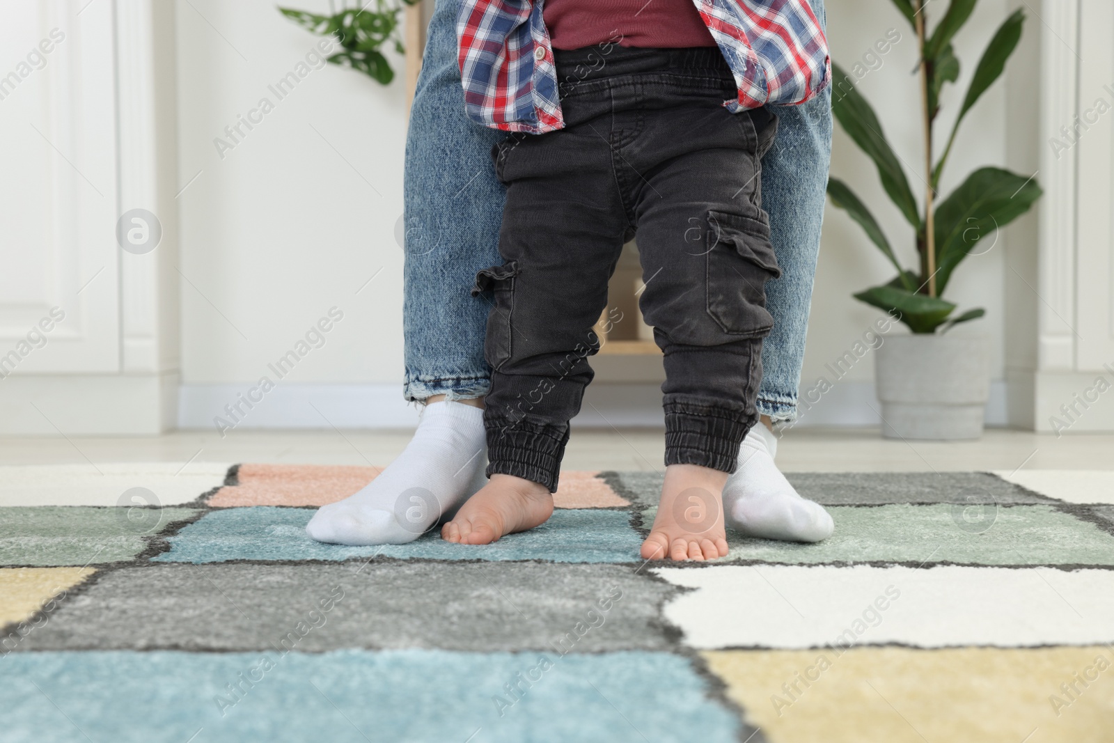 Photo of Mother supporting her son while he learning to walk on carpet indoors, closeup