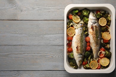 Photo of Delicious fish with vegetables and lemon in baking dish on grey wooden table, top view. Space for text