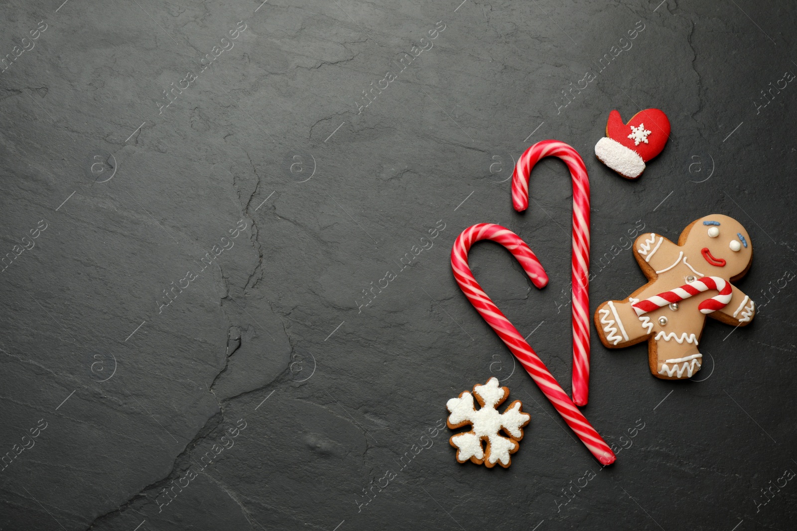 Photo of Tasty candy canes and gingerbread cookies on black table, flat lay. Space for text