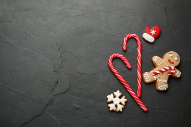 Tasty candy canes and gingerbread cookies on black table, flat lay. Space for text