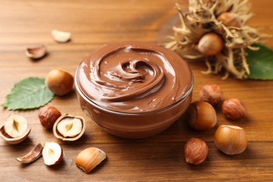 Glass bowl with tasty chocolate hazelnut spread and nuts on wooden table