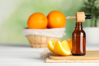 Photo of Bottle of essential oil, pipette and orange on white wooden table, space for text