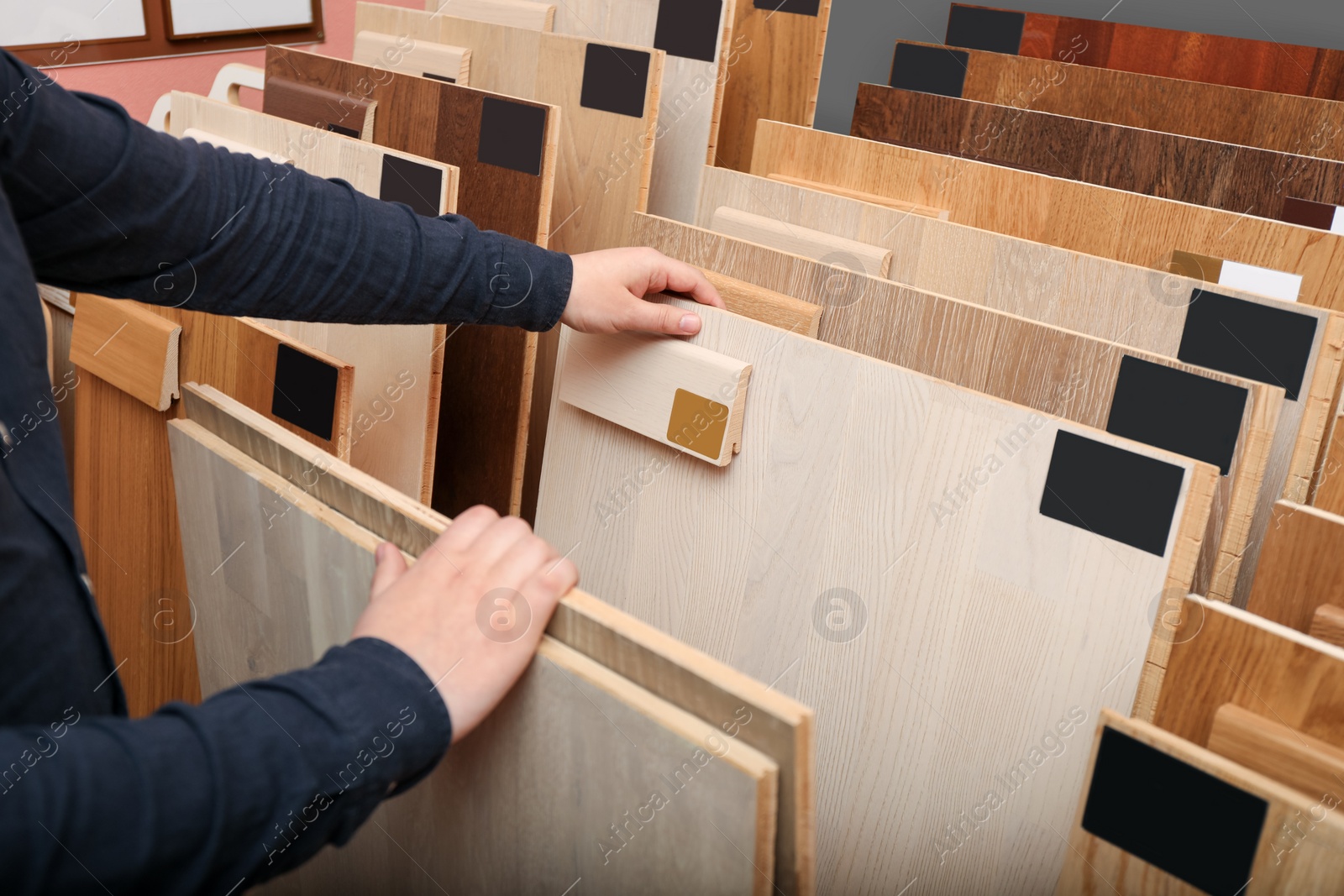 Photo of Man choosing wooden flooring among different samples in shop, closeup