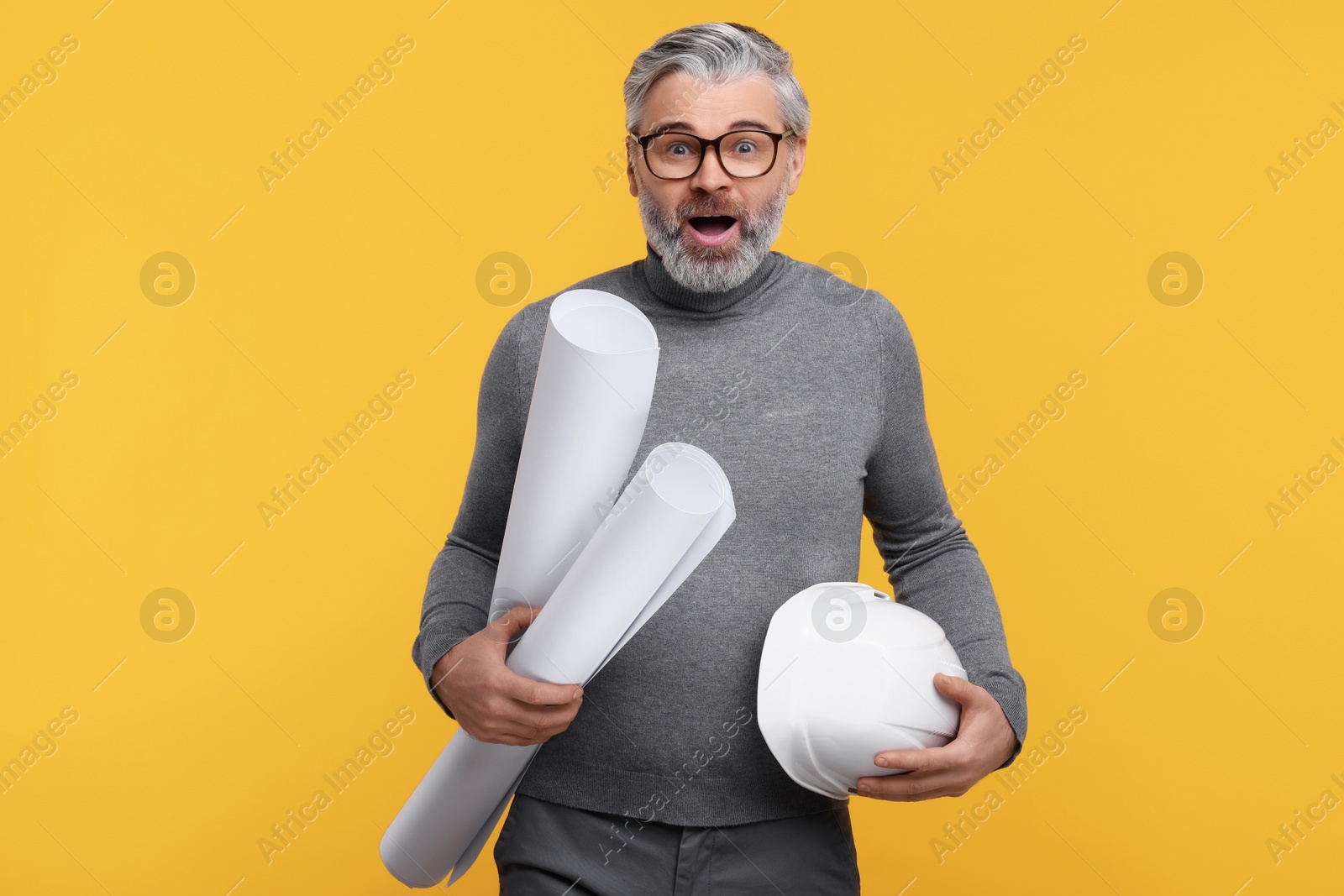 Photo of Emotional architect with hard hat and drafts on orange background