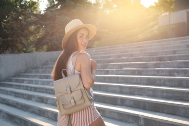 Photo of Beautiful young woman with stylish backpack and hat on stairs outdoors