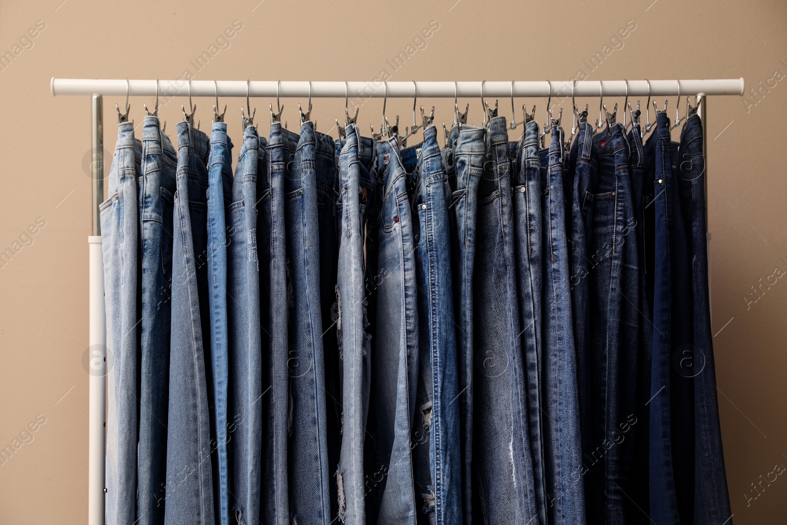 Photo of Rack with stylish jeans on beige background