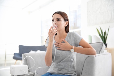 Young woman with asthma machine in light room