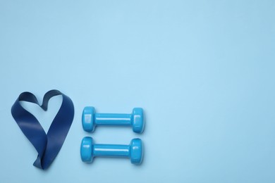 Photo of Two dumbbells and fitness elastic band in shape of heart on light blue background, flat lay. Space for text