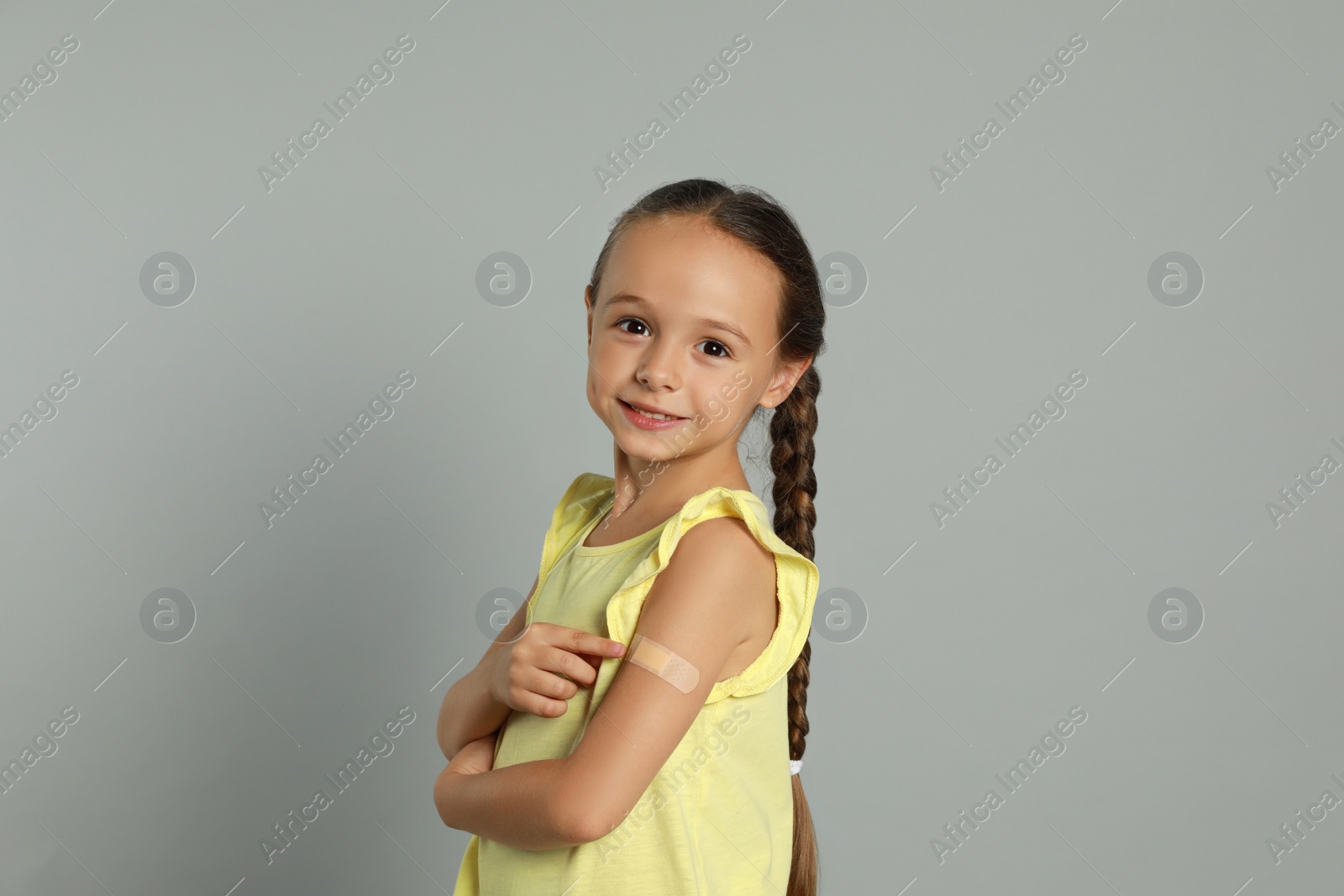 Photo of Vaccinated little girl showing medical plaster on her arm against light grey background