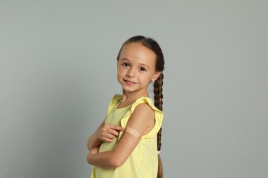 Vaccinated little girl showing medical plaster on her arm against light grey background