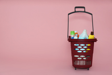 Shopping basket full of cleaning supplies on pink background. Space for text