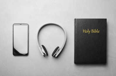 Photo of Bible, phone and headphones on light grey background, flat lay. Religious audiobook
