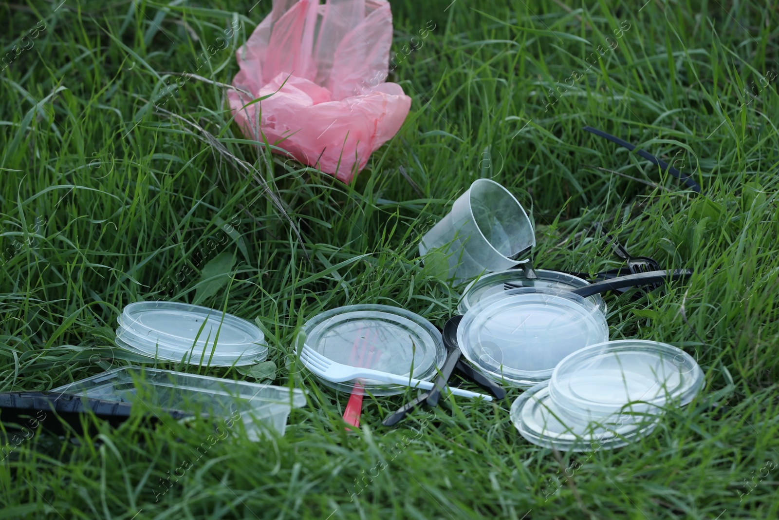 Photo of Used plastic tableware and bag on grass outdoors. Environmental pollution concept