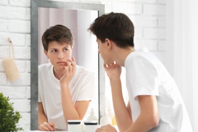 Photo of Teenage boy with acne problem looking in mirror at home