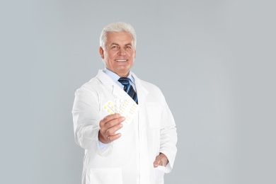 Photo of Senior pharmacist with pills on light grey background