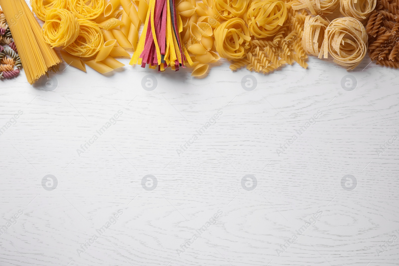 Photo of Different types of pasta on white wooden table, flat lay. Space for text