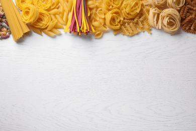 Different types of pasta on white wooden table, flat lay. Space for text