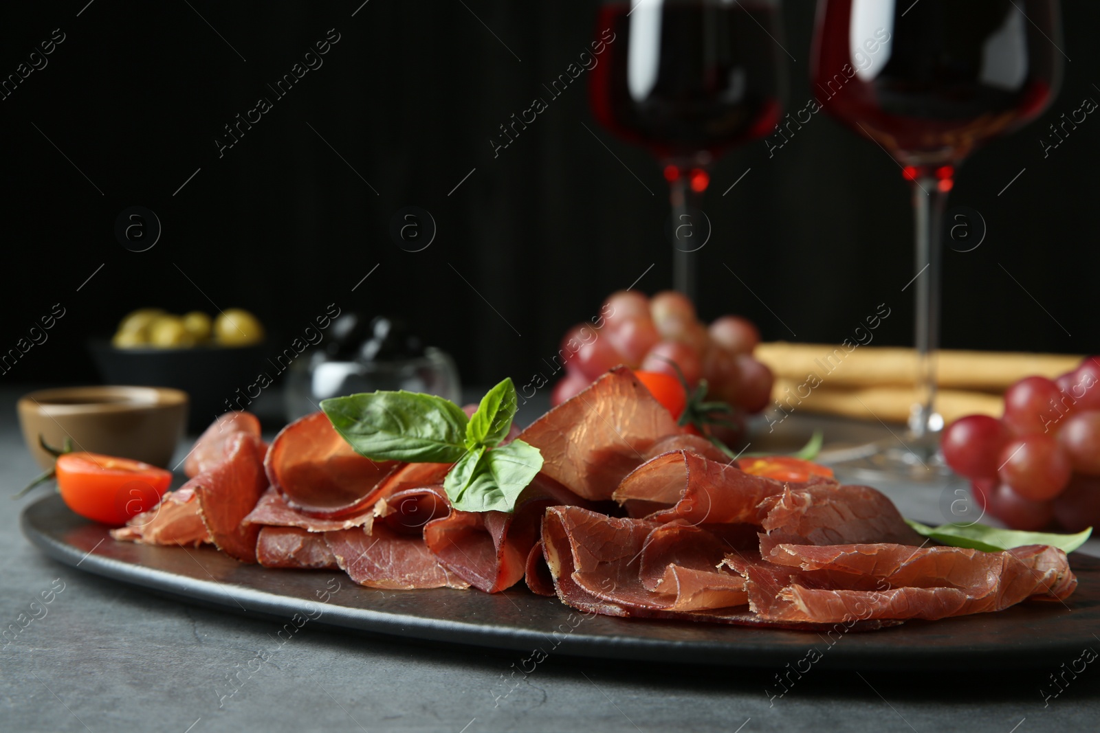 Photo of Delicious bresaola, tomato and basil leaves on grey textured table