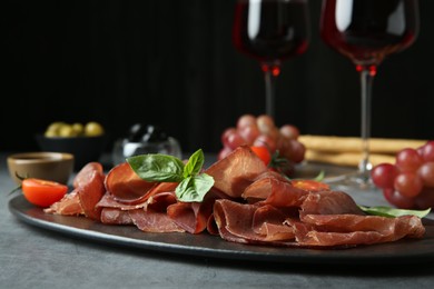 Photo of Delicious bresaola, tomato and basil leaves on grey textured table